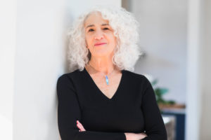 Image of Deborah Meyer smiling, wearing a black shirt, and leaning against a white wall