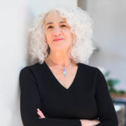 Image of Deborah Meyer smiling, wearing a black shirt, and leaning against a white wall
