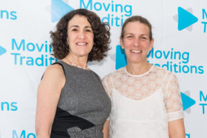 Deborah Meyer and Sally Gottesman standing in front of a backdrop of Moving Traditions logos